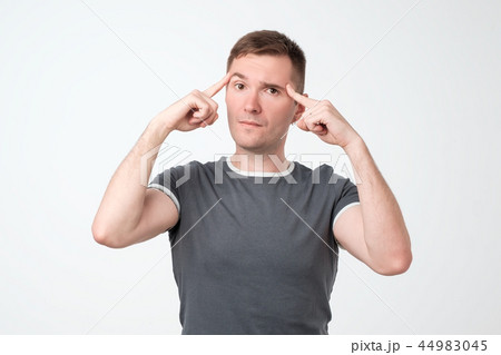 Unhappy puzzled young man pointing at his head with fingers and looking at camera. Unhappy puzzled young man pointing at his head with fingers and looking at camera. 44983045