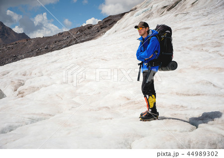 Traveler in a cap and sunglasses with a backpack on his shoulders in the snowy mountains on the 44989302