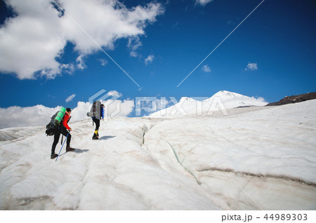 Two tourists, a man and a woman with backpacks and crampons on their feet walk along the glacier Two tourists, a man and a woman with backpacks and crampons on their feet walk along the glacier 44989303