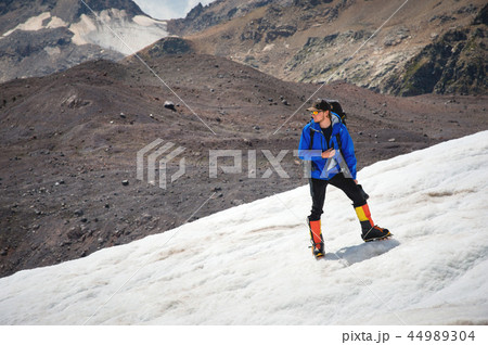 A mountaineer with a backpack walks in wheelchairs, stands on a dusty glacier with sneakers in the A mountaineer with a backpack walks in wheelchairs, stands on a dusty glacier with sneakers in the 44989304