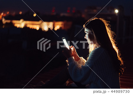 Young girl sits at night on the roof of a house. Beautiful evening Young girl sits at night on the roof of a house. Beautiful evening 44989730