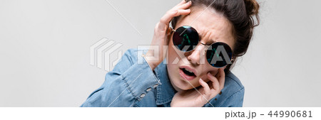 Young brunette girl in round glasses. Hairs are gathered in a bun. The girl put her hand to her head Young brunette girl in round glasses. Hairs are gathered in a bun. The girl put her hand to her head 44990681