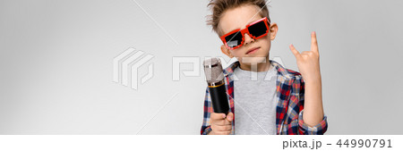 A handsome boy in a plaid shirt, gray shirt and jeans stands on a gray background. A boy wearing A handsome boy in a plaid shirt, gray shirt and jeans stands on a gray background. A boy wearing 44990791