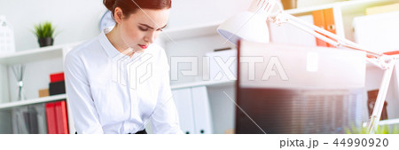 A young girl in the office is standing near the table, holding a pencil and a calculator in her hand A young girl in the office is standing near the table, holding a pencil and a calculator in her hand 44990920