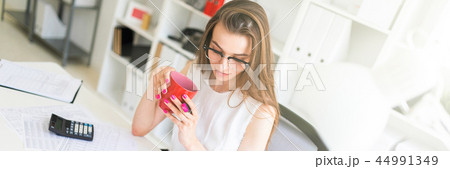 A young girl in the office holds a pink marker, a red mug and works with documents. A young girl in the office holds a pink marker, a red mug and works with documents. 44991349