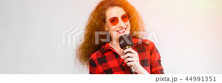 Portrait of beautiful redhead happy young woman in sunglasses smiling holding microphone on gray Portrait of beautiful redhead happy young woman in sunglasses smiling holding microphone on gray 44991351