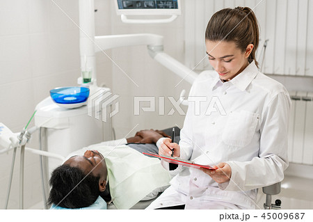 Charming beautiful girl doctor dentist. Young African American male patient at chair at dental Charming beautiful girl doctor dentist. Young African American male patient at chair at dental 45009687