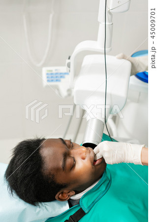 Woman dentist using x ray machine, patient lying on chair in dentistry. Young African American male 45009701