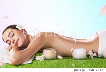Beautiful young woman lying on green towel at spa center. 45012014