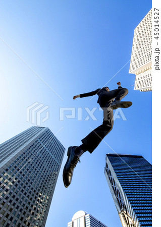 ビル街を青空バックにジャンプするスーツ姿のビジネスマン1人。挑戦,努力,成功,元気イメージ 45014527