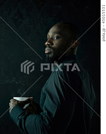 Stylish young black man with cup of coffee posing on dark background. Stylish young black man with cup of coffee posing on dark background. 45015531
