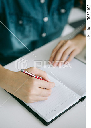 woman's hand with pen writing on book 45022402