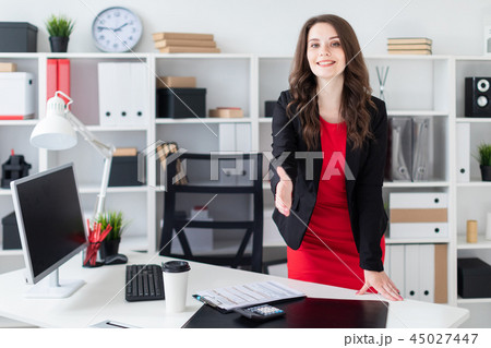 A young girl stands in the office near the table and stretches her hand forward A young girl stands in the office near the table and stretches her hand forward 45027447