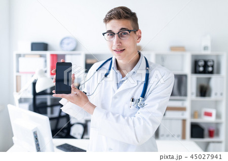 A young man in a white robe standing in the office and holding a phone. A young man in a white robe standing in the office and holding a phone. 45027941