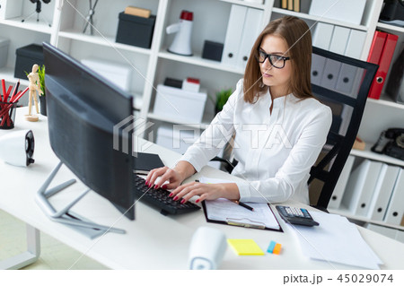 Young girl sitting at the table and working with a computer, documents and calculator Young girl sitting at the table and working with a computer, documents and calculator 45029074