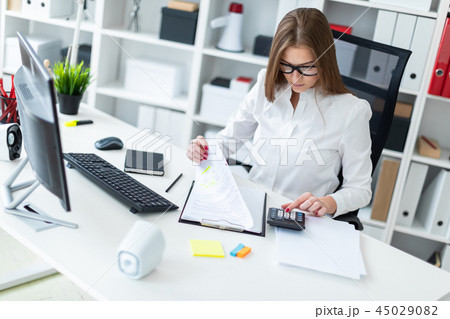Young girl sitting at the table and working with a computer, documents and calculator Young girl sitting at the table and working with a computer, documents and calculator 45029082