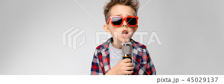 A handsome boy in a plaid shirt, gray shirt and jeans stands on a gray background. A boy wearing A handsome boy in a plaid shirt, gray shirt and jeans stands on a gray background. A boy wearing 45029137