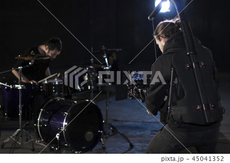 Professional videographer holding camera mounted on easy rig and filming a drummer. Videographer 45041352