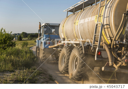 A blue tractor with a tank rides along a road in a wheat field. A blue tractor with a tank rides along a road in a wheat field. 45043717