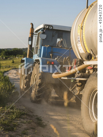 A blue tractor with a tank rides along a road in a wheat field. 45043720