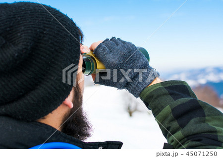 Man using binoculars on snow covered mountain 45071250