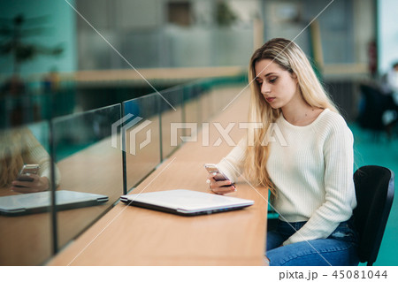 Blonde girl use phone in library. sudent sist on stool by the window Blonde girl use phone in library. sudent sist on stool by the window 45081044