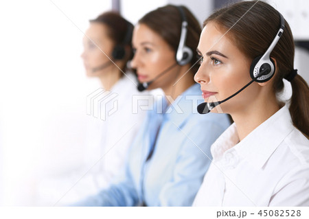 Group of callcenter operators at work. Focus at beautiful business woman in headset Group of callcenter operators at work. Focus at beautiful business woman in headset 45082528