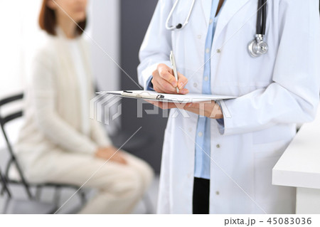 Doctor woman filling up medical form while standing near reception desk at clinic or emergency 45083036
