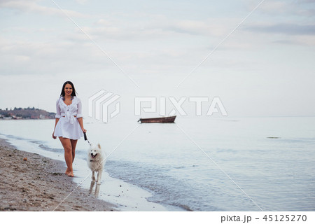 Beautiful brunette woman on the beach with a dog walking Beautiful brunette woman on the beach with a dog walking 45125270