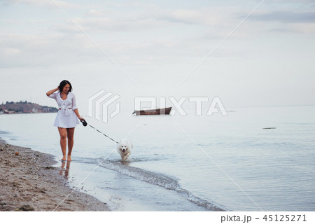 Beautiful brunette woman on the beach with a dog walking Beautiful brunette woman on the beach with a dog walking 45125271