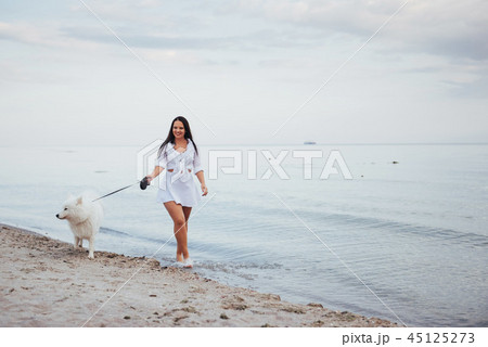 Beautiful brunette woman on the beach with a dog walking 45125273