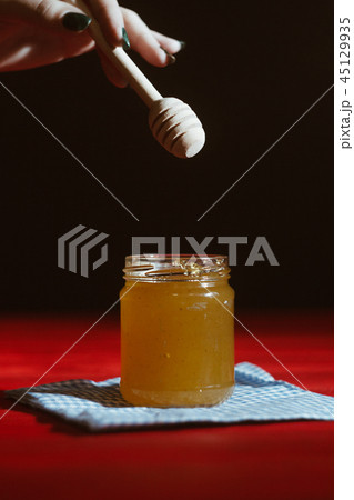 Honey in a glass jar close up on a black background on a red wooden table. pour honey with a stick Honey in a glass jar close up on a black background on a red wooden table. pour honey with a stick 45129935