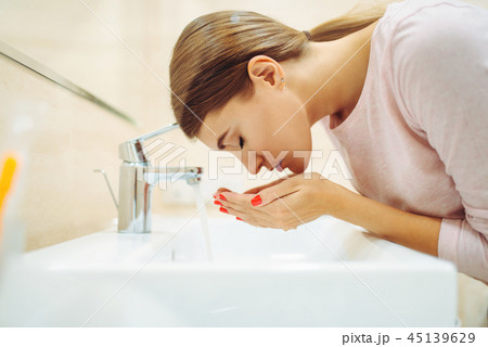 Woman washes her face at the sink in bathroom 45139629