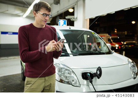 Man is holding a phone. His electric car charged  45143083