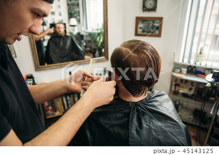 Master cuts hair and beard of men in the barbershop, hairdresser makes hairstyle for a young man Master cuts hair and beard of men in the barbershop, hairdresser makes hairstyle for a young man 45143125