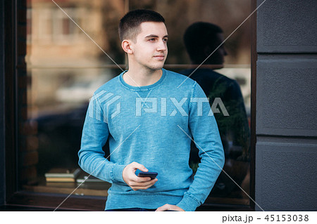 Young man is using the phone on the street. Handsome guy stand in front of window 45153038