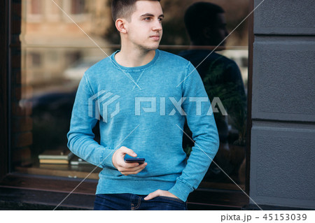Young man is using the phone on the street. Handsome guy stand in front of window 45153039