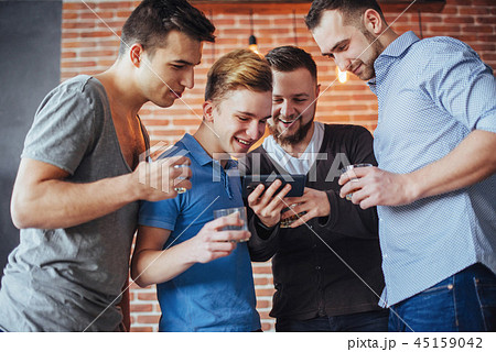 Cheerful old friends communicate with each other and phone watch,  glasses of whiskey in pub. Concep 45159042
