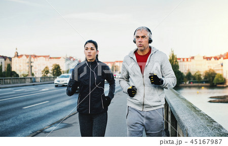 A fit couple with headphones running outdoors on the bridge in Prague city. A fit couple with headphones running outdoors on the bridge in Prague city. 45167987