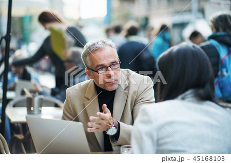 Man and woman business partners with laptop sitting in a cafe in city, talking. Man and woman business partners with laptop sitting in a cafe in city, talking. 45168103