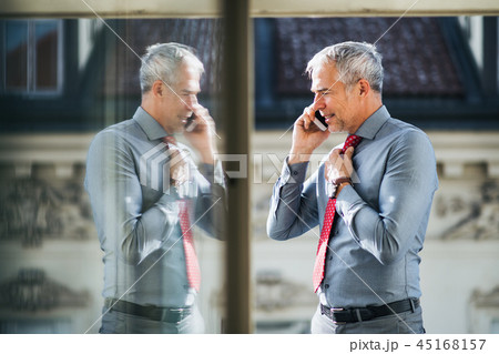Mature businessman with smartphone standing on a terrace in city, making a phone call. Mature businessman with smartphone standing on a terrace in city, making a phone call. 45168157