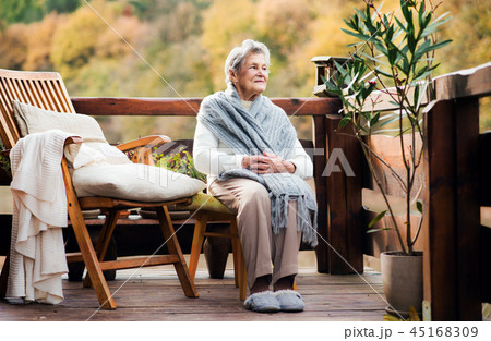 An elderly woman sitting outdoors on a terrace on a sunny day in autumn. 45168309