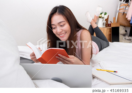 Asian woman wear pink vest lying on bed reading Asian woman wear pink vest lying on bed reading 45169335