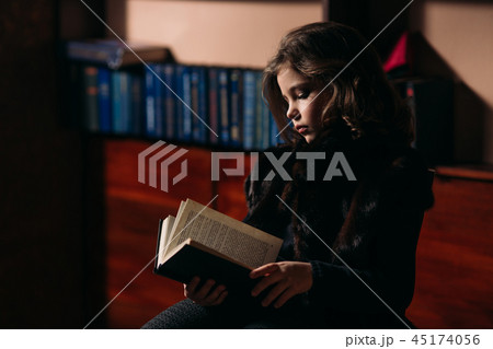 Beautiful little girl is reading a book in the library. 45174056