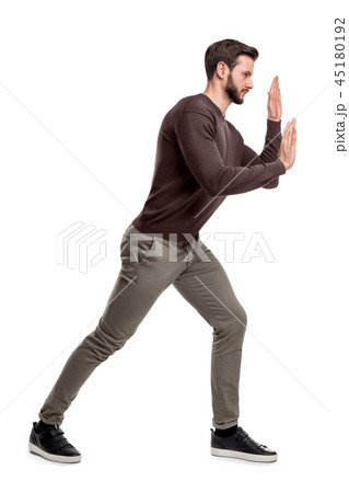 A bearded fit man in casual pants presses his hands over an invisible object in order to move it. A bearded fit man in casual pants presses his hands over an invisible object in order to move it. 45180192
