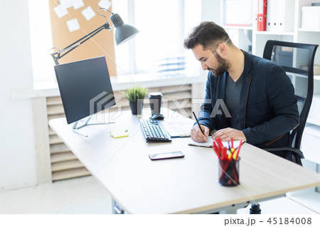 The young man works in the office at a computer Desk with documents, diagrams and phone. The young man works in the office at a computer Desk with documents, diagrams and phone. 45184008
