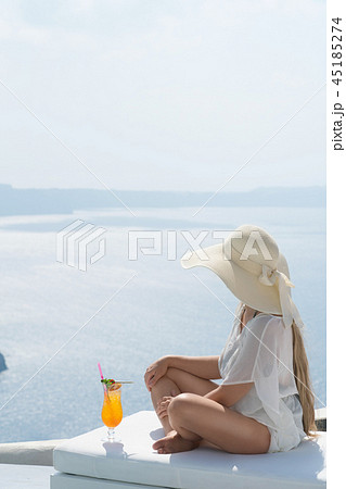 young woman drinking a cocktail enjoying a magnificent view of Santorini near the pool young woman drinking a cocktail enjoying a magnificent view of Santorini near the pool 45185274