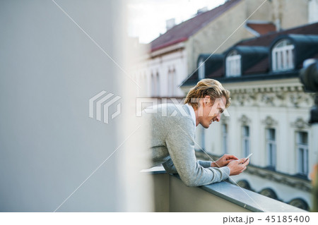 Young man with smartphone standing on a balcony in city, texting. Young man with smartphone standing on a balcony in city, texting. 45185400