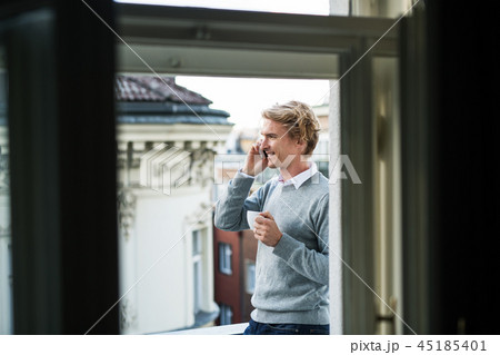 Young man with smartphone standing on a balcony in city, making a phone call. 45185401
