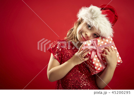 adorable little girl in a Christmas dress in a Santa's hat with a christmas gift 45200295